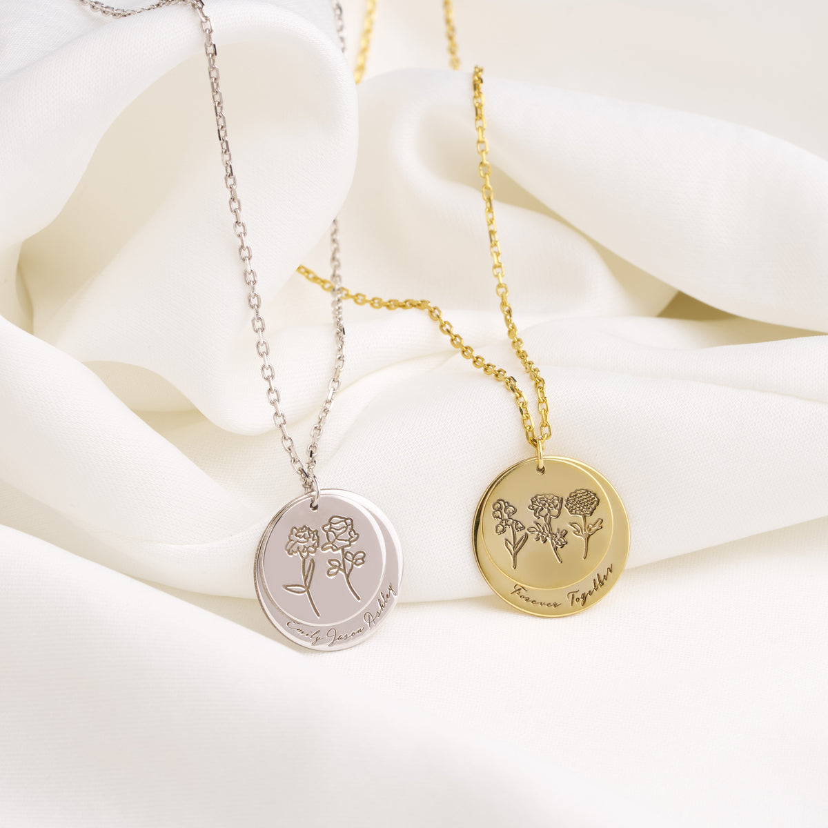 Silver and gold birth flower disc necklaces laid on soft white fabric