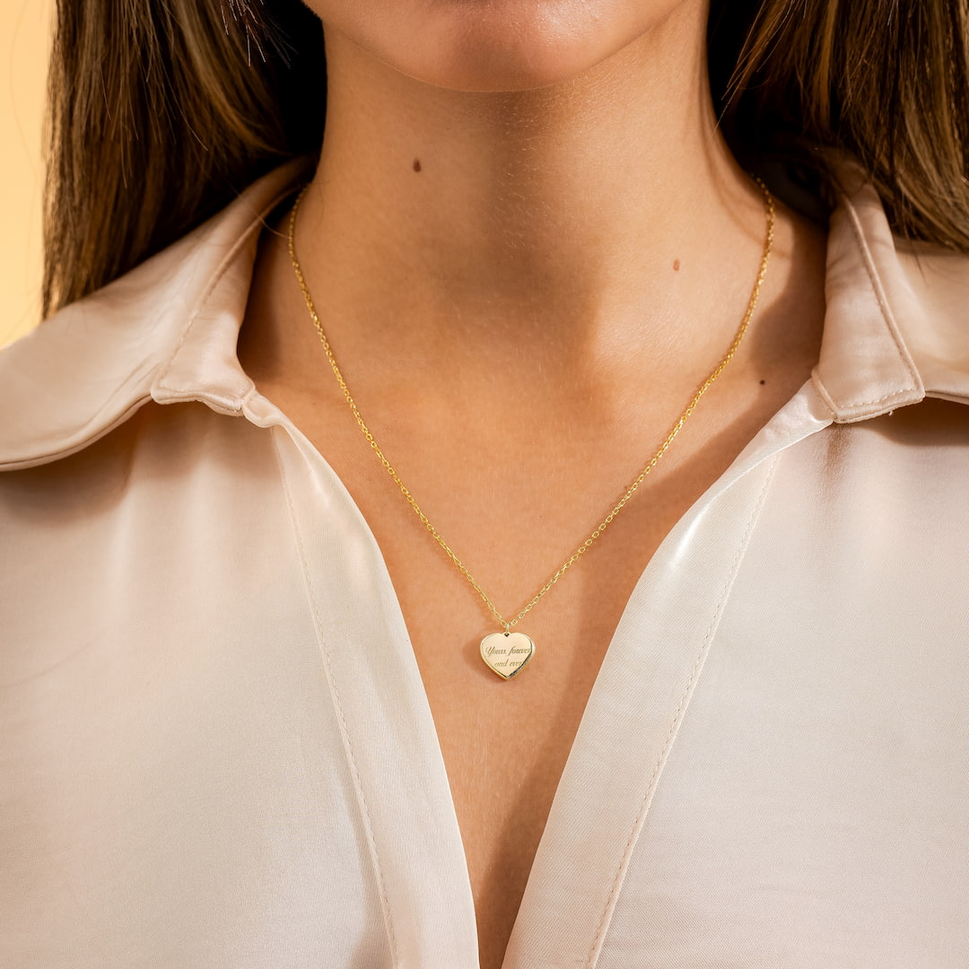 Gold necklace with a heart pendant worn by a person in a light-colored shirt.