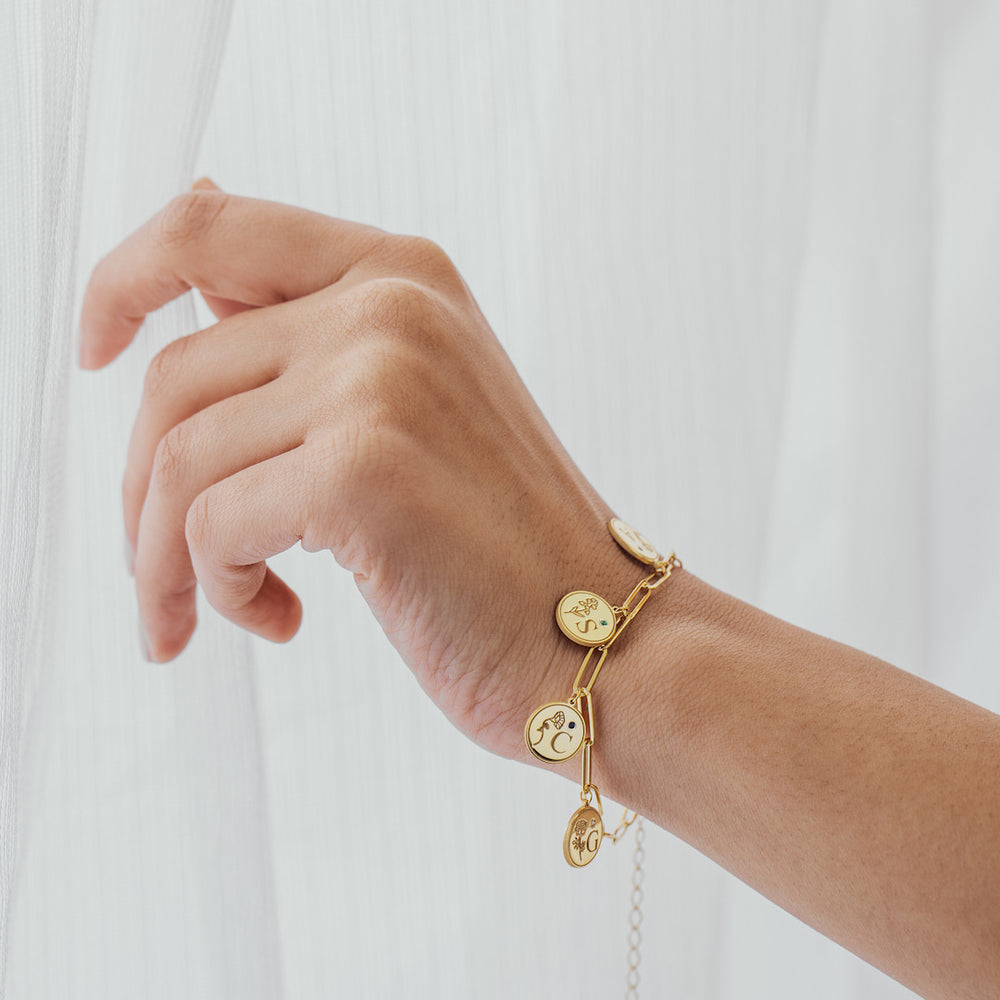 Gold bracelet with charms on a wrist against a white background