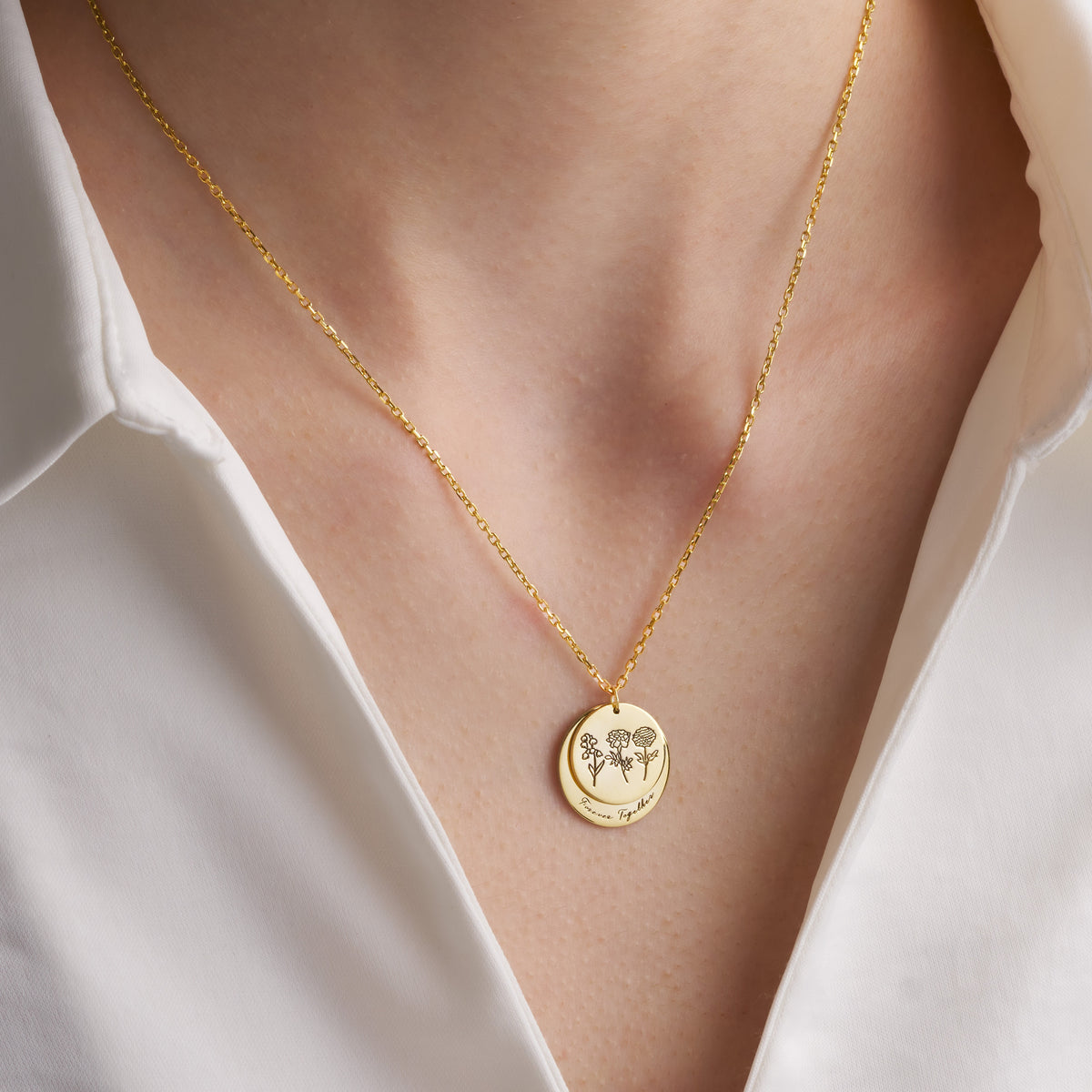 Gold birth flower double disc necklace worn at the collarbone with an open white shirt