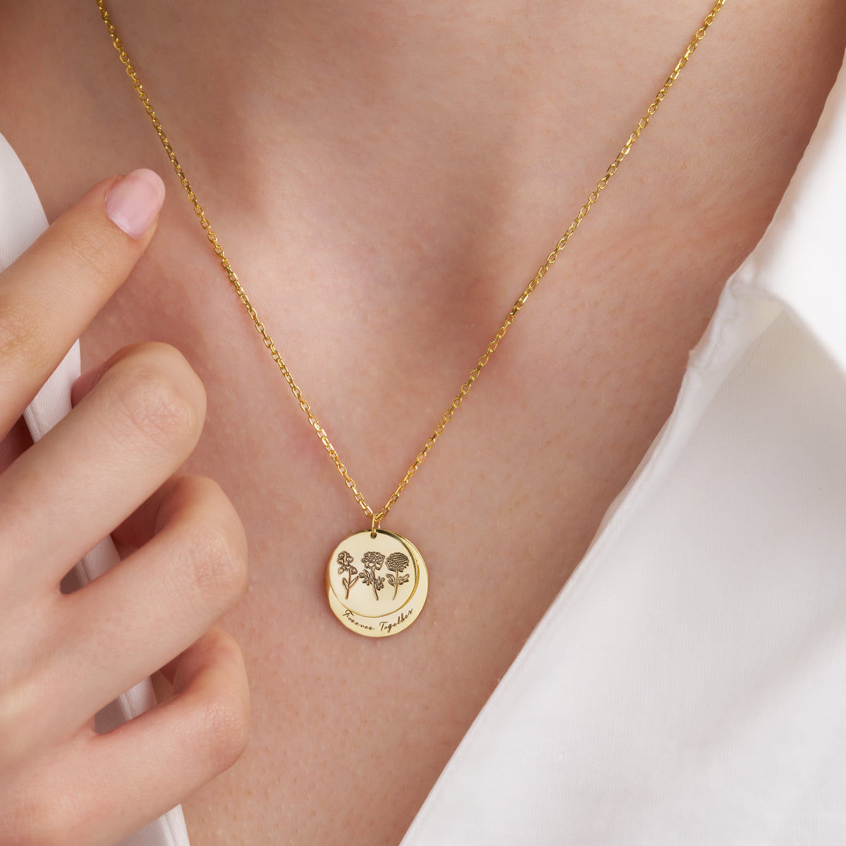 Model wearing the gold birth flower double disc necklace, fingertips holding the chain
