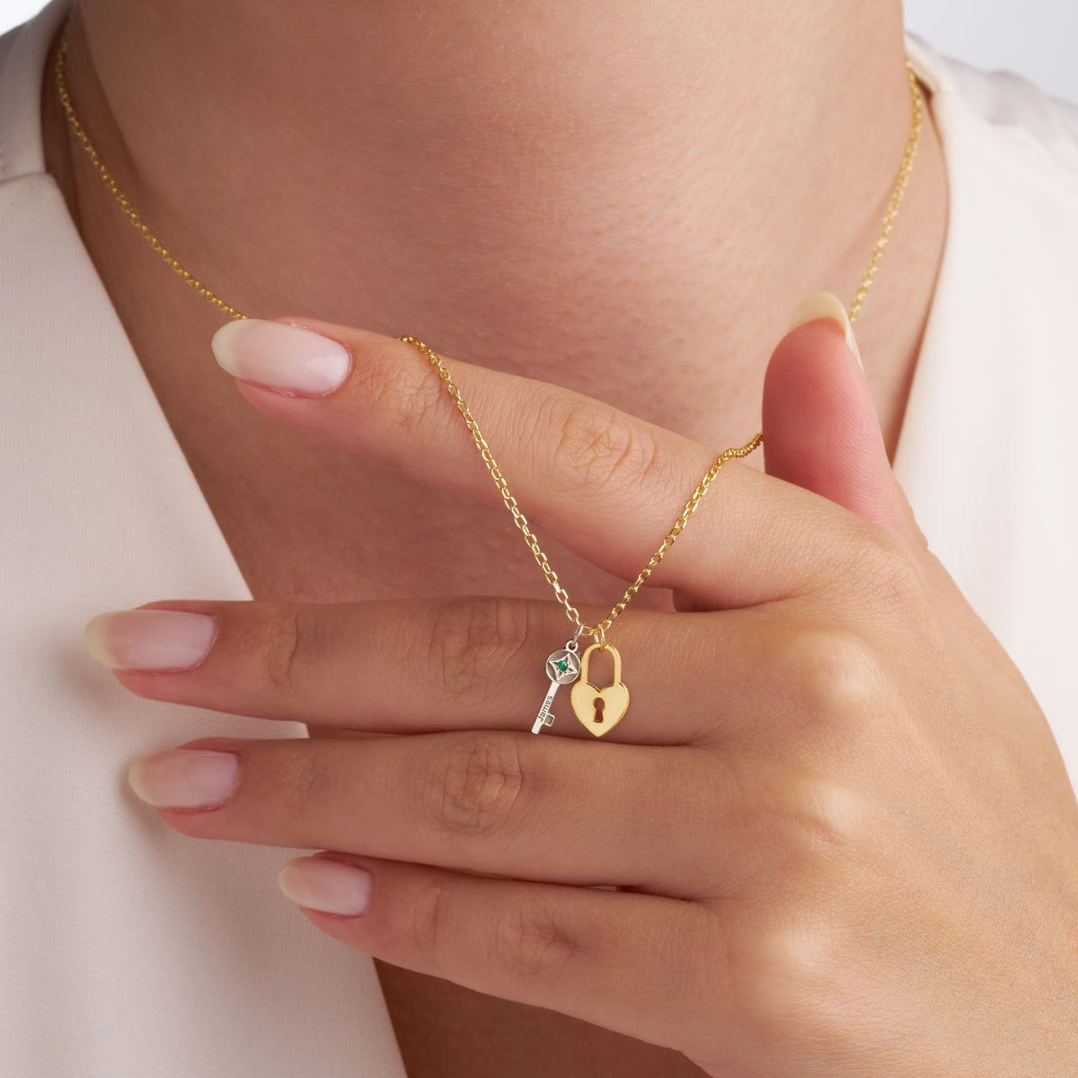 Hand holding the chain of the gold heart lock and silver birthstone key necklace