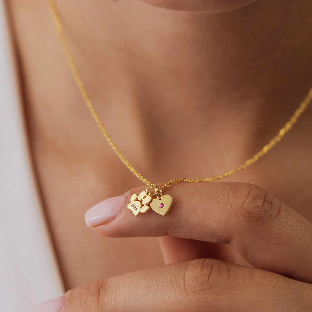 Gold necklace with heart and paw print charms held by a hand against a neutral background
