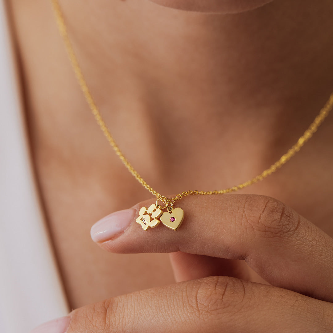 Gold necklace with heart and paw print charms held by a hand against a neutral background