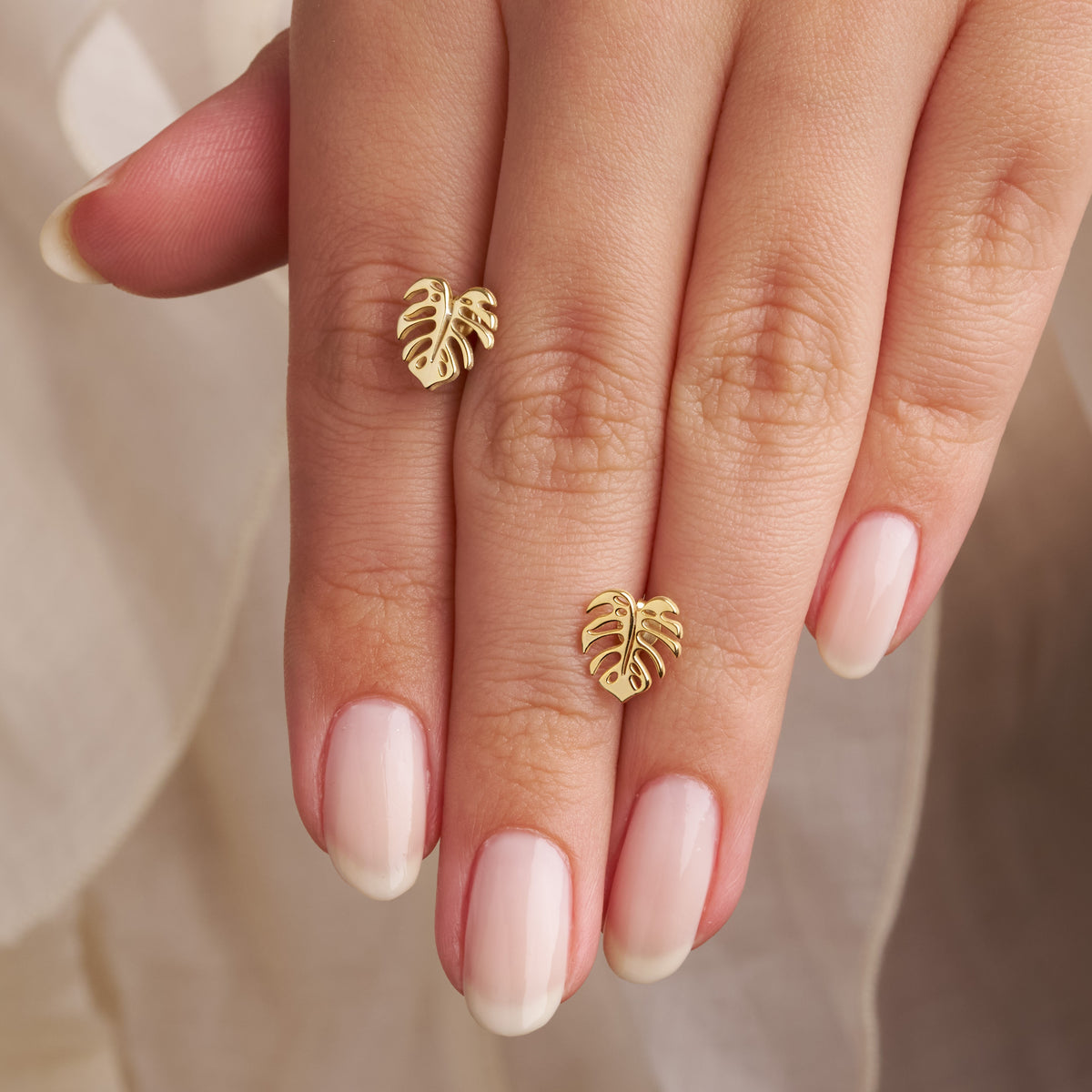 Pair of gold monstera leaf stud earrings with cut-out details on a travertine stone