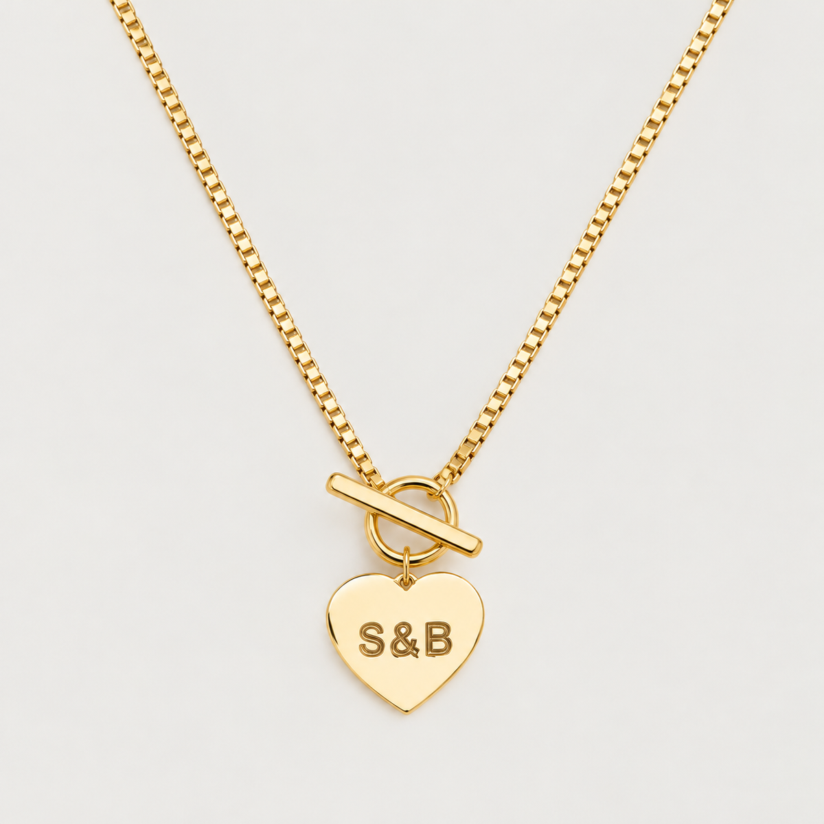 Gold engraved heart toggle necklace, studio image on a cream background