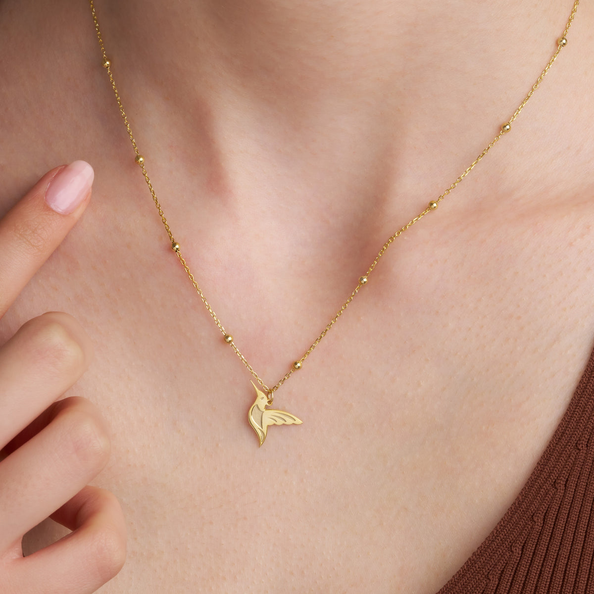 Close-up of a gold hummingbird necklace worn at the collarbone