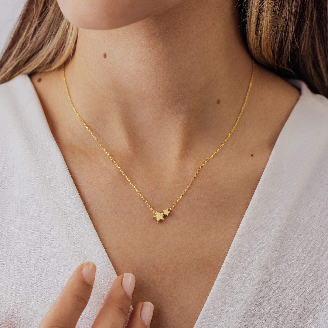 Gold necklace with star pendant on a person wearing a white top