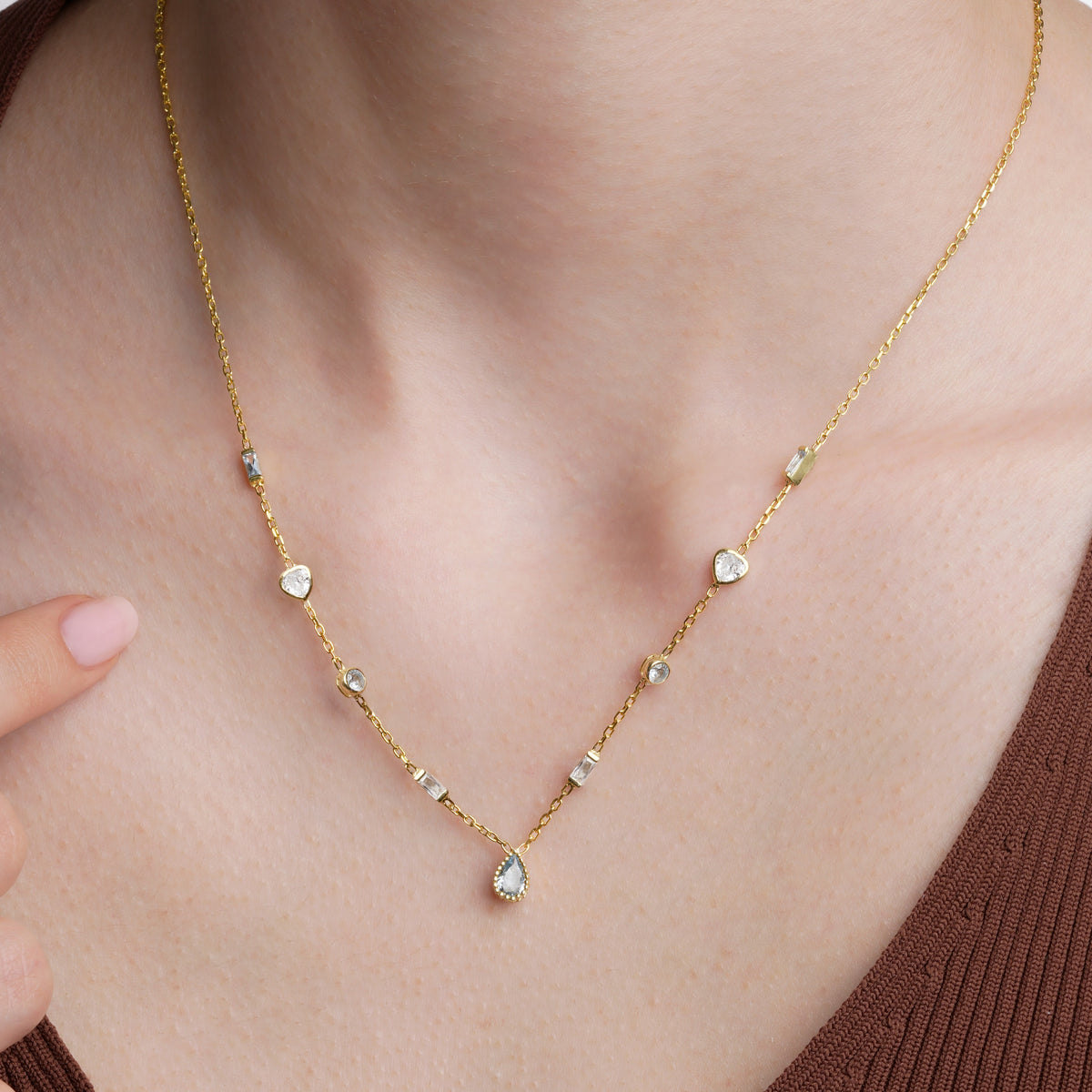 Gold multiple birthstone necklace worn with clear and light blue stones and a light blue teardrop pendant