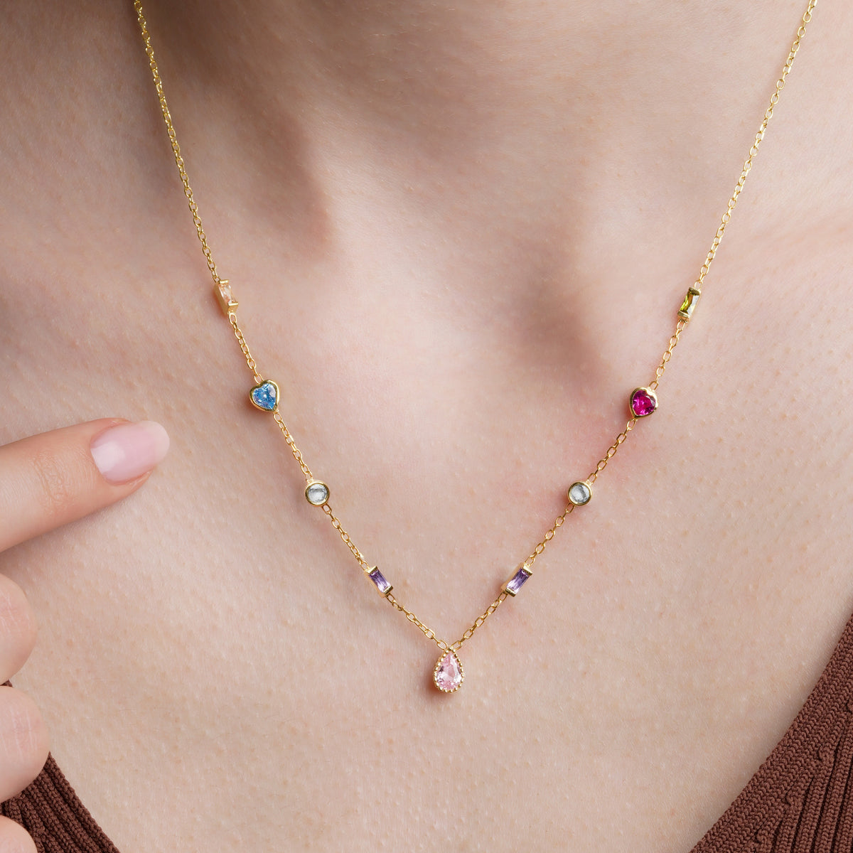 Close-up of a gold multiple birthstone necklace on the collarbone with blue and magenta hearts and a pink teardrop