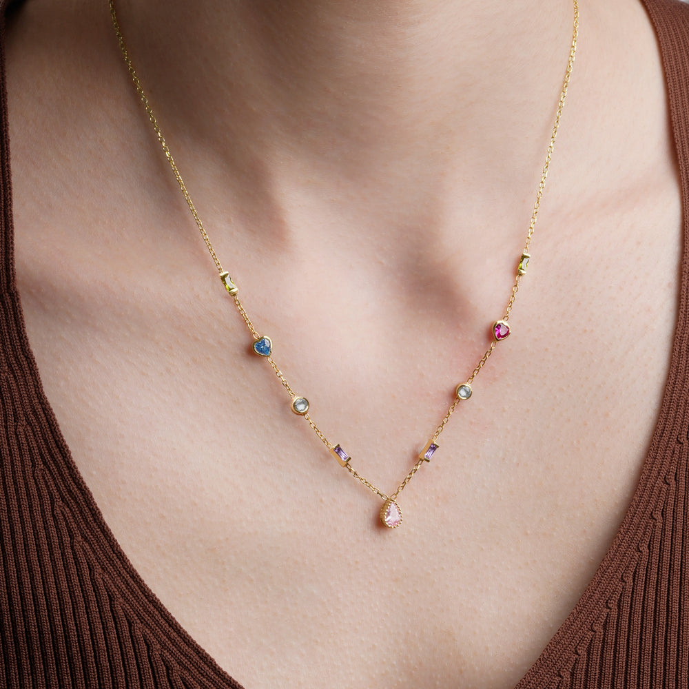 Gold multiple birthstone necklace worn on the neck, with heart, round, baguette and teardrop stones in mixed colors