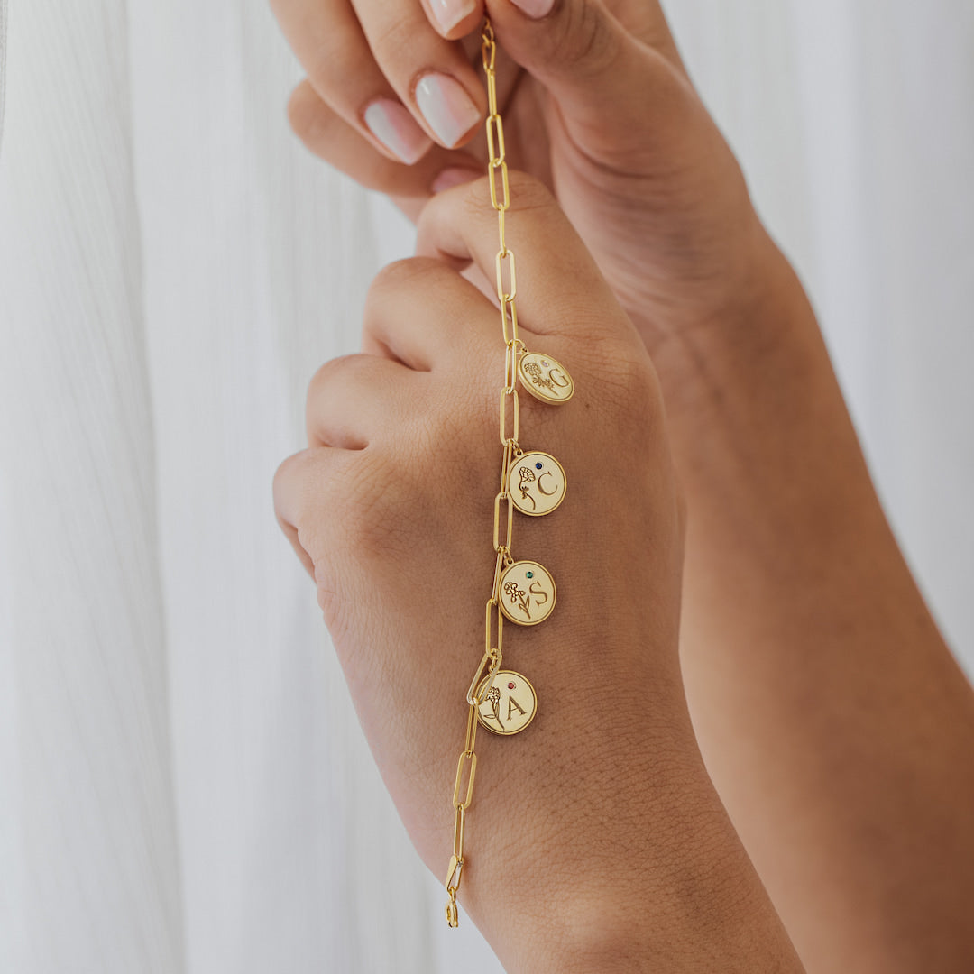Gold bracelet with circular charms on a person's wrist against a white background