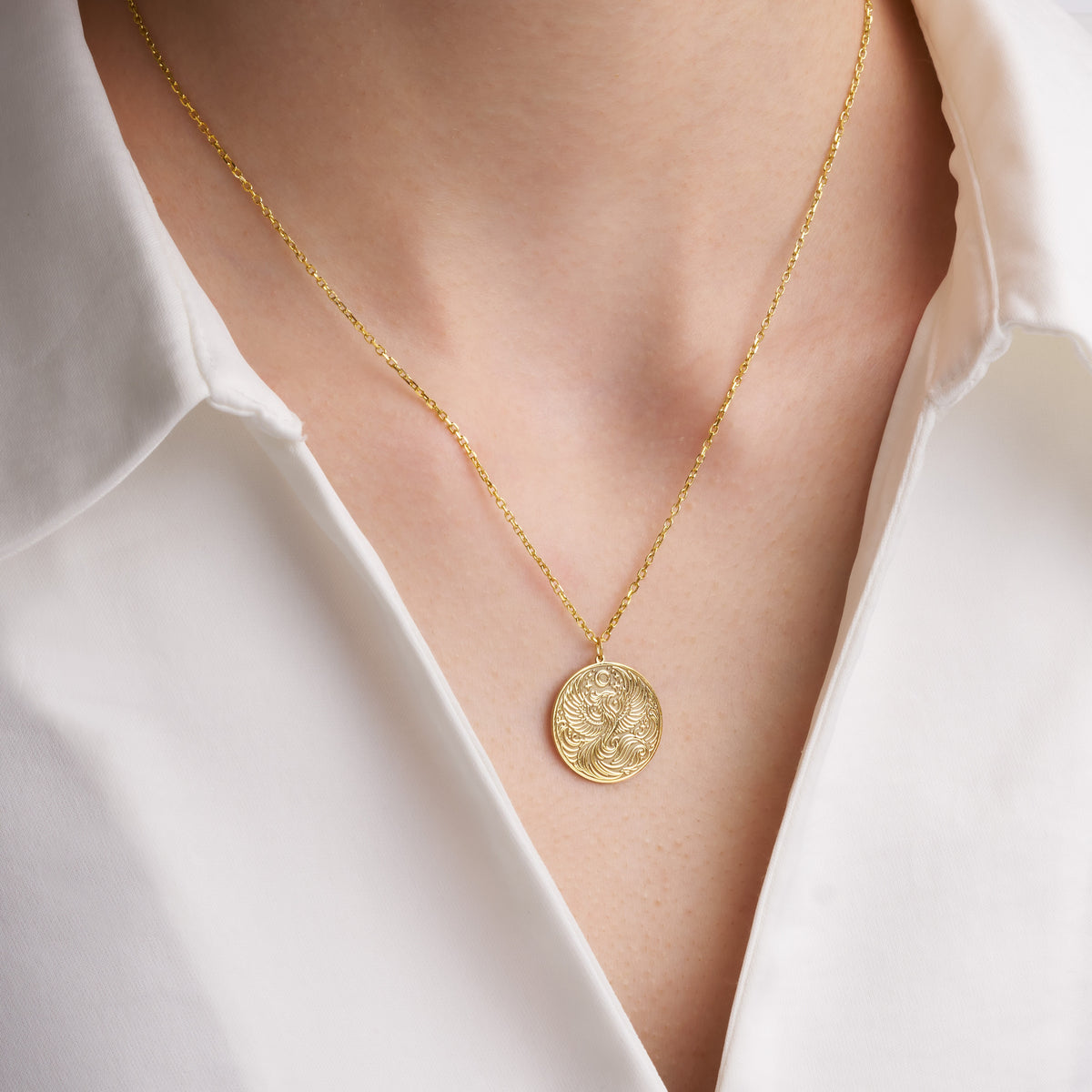 Gold phoenix disc pendant necklace worn with an open white collar shirt
