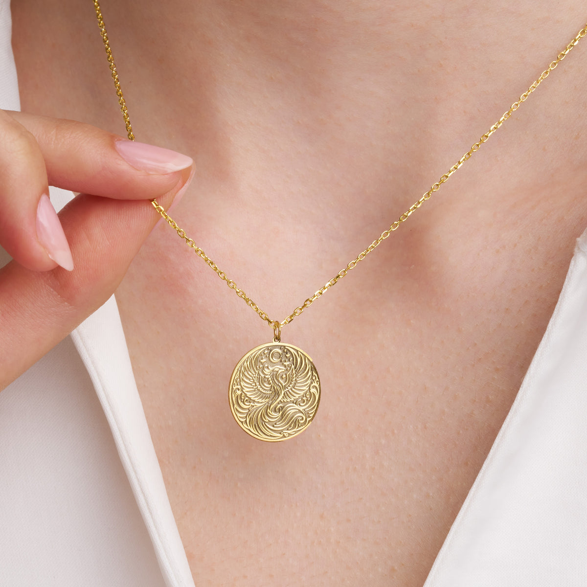 Woman wearing a gold phoenix pendant necklace, holding the cable chain
