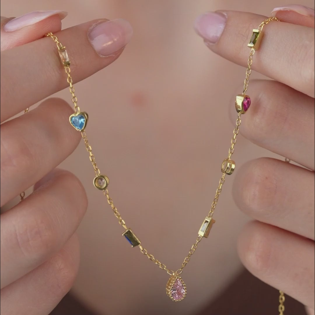 Video of a gold multiple birthstone necklace held in the fingers, then worn, showing its colored stones