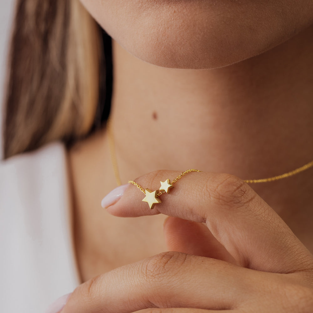 Close-up of a person wearing a gold necklace with star pendants.