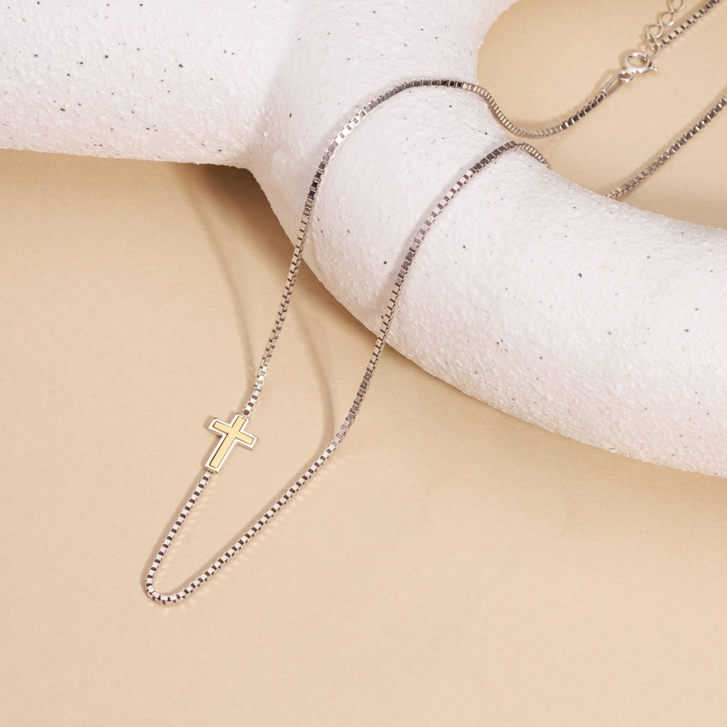 Two-tone cross necklace draped over a white textured stand, showing the spring ring clasp and extender chain