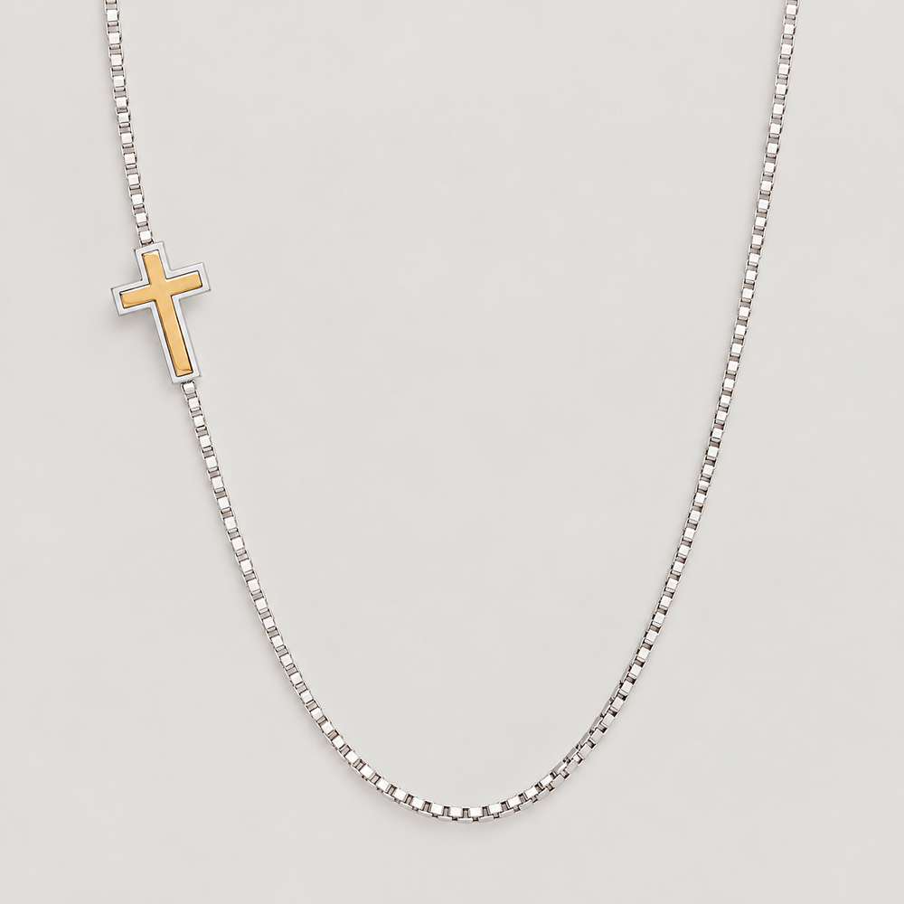 Two-tone sideways cross necklace laid flat on light gray: gold-tone cross in a silver frame on a box chain