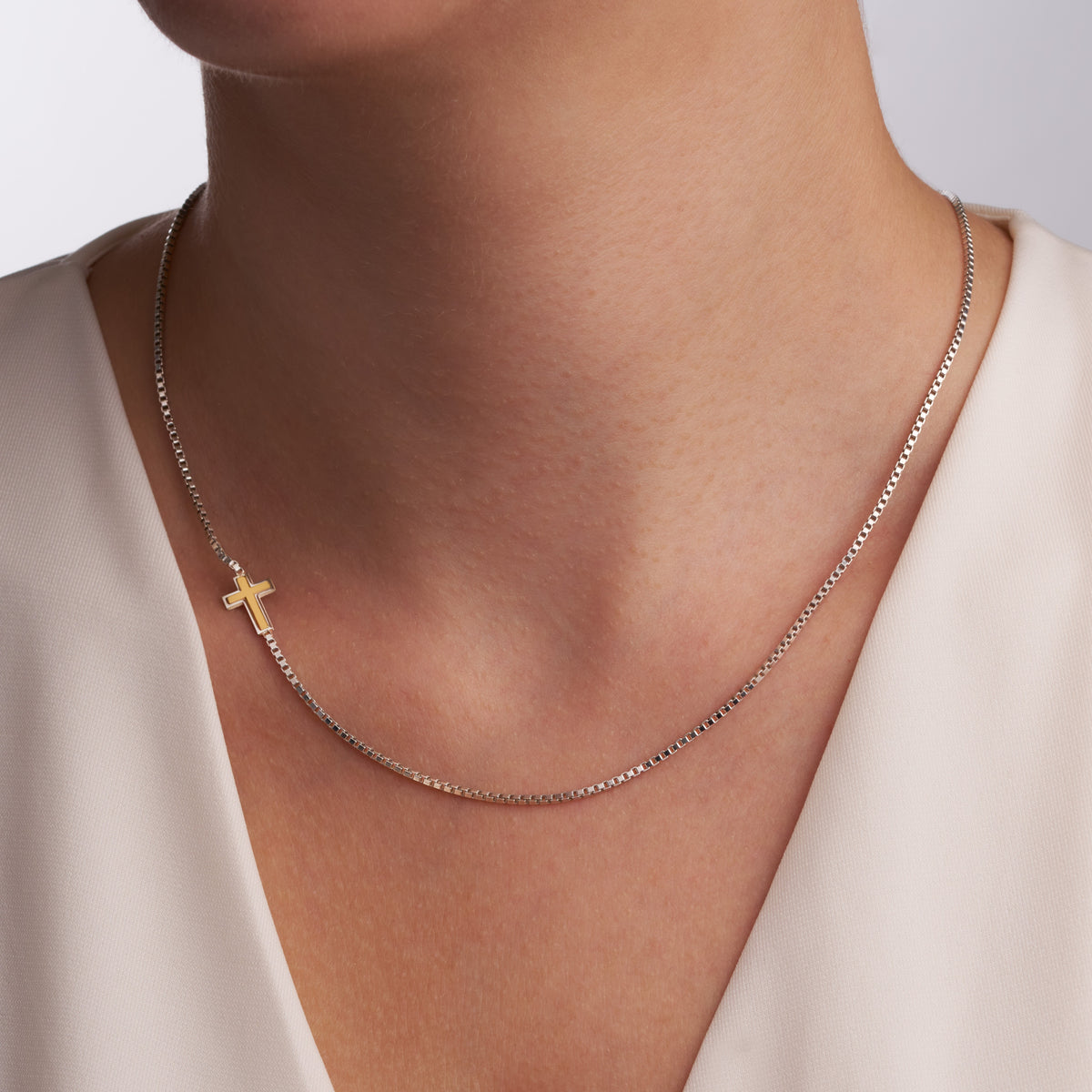 Woman wearing the two-tone sideways cross necklace, the cross resting off-center near the collarbone on a box chain